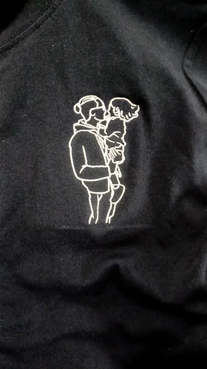 Kunde zeigt schwarzes bestickes T-Shirt mit Opa, der den Enkel im Arm hält